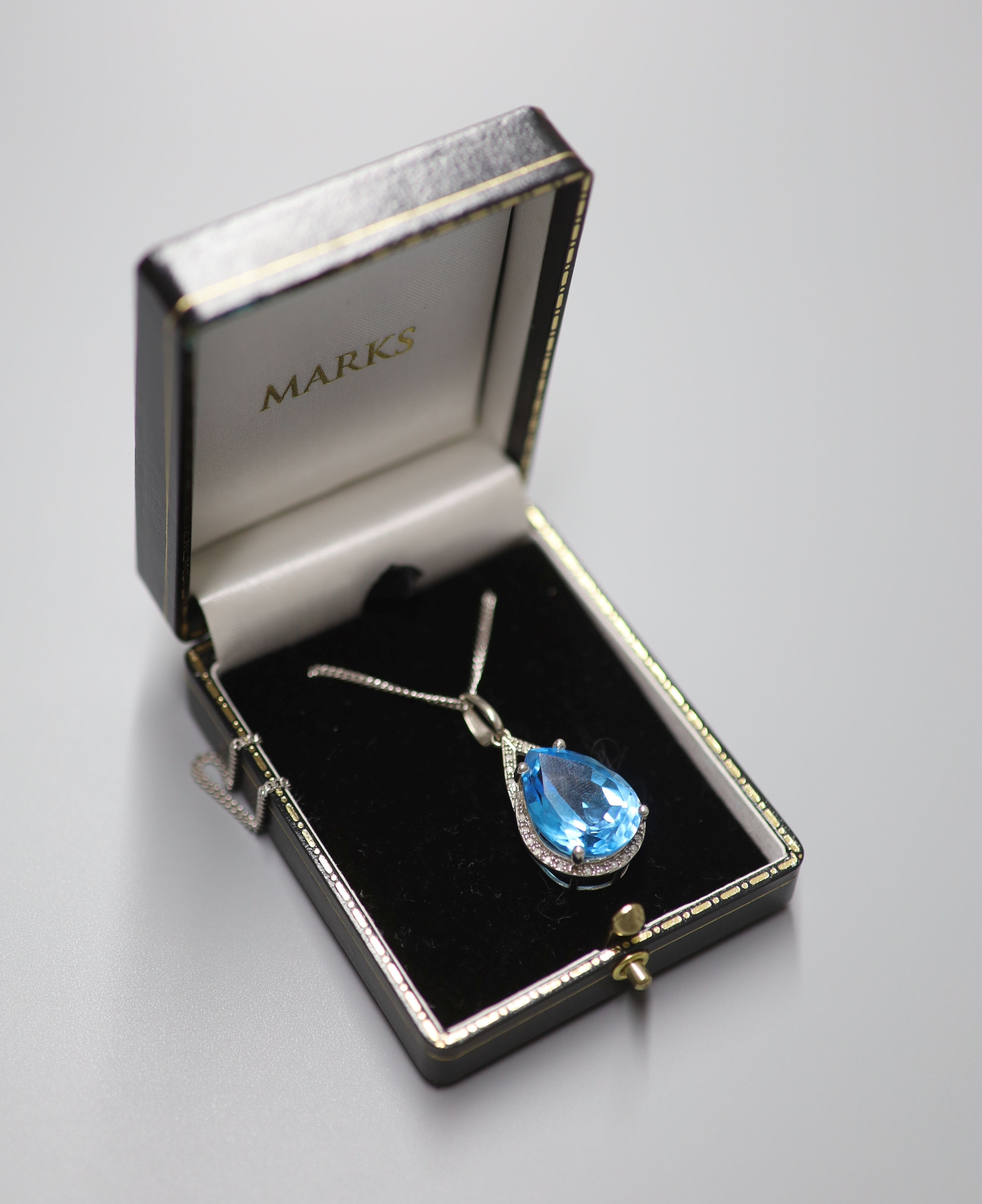 A modern white metal (stamped 9k), blue topaz and diamond chip set pendant, 29mm, on a 9ct white gold chain, 44cm, gross weight 12.3 grams